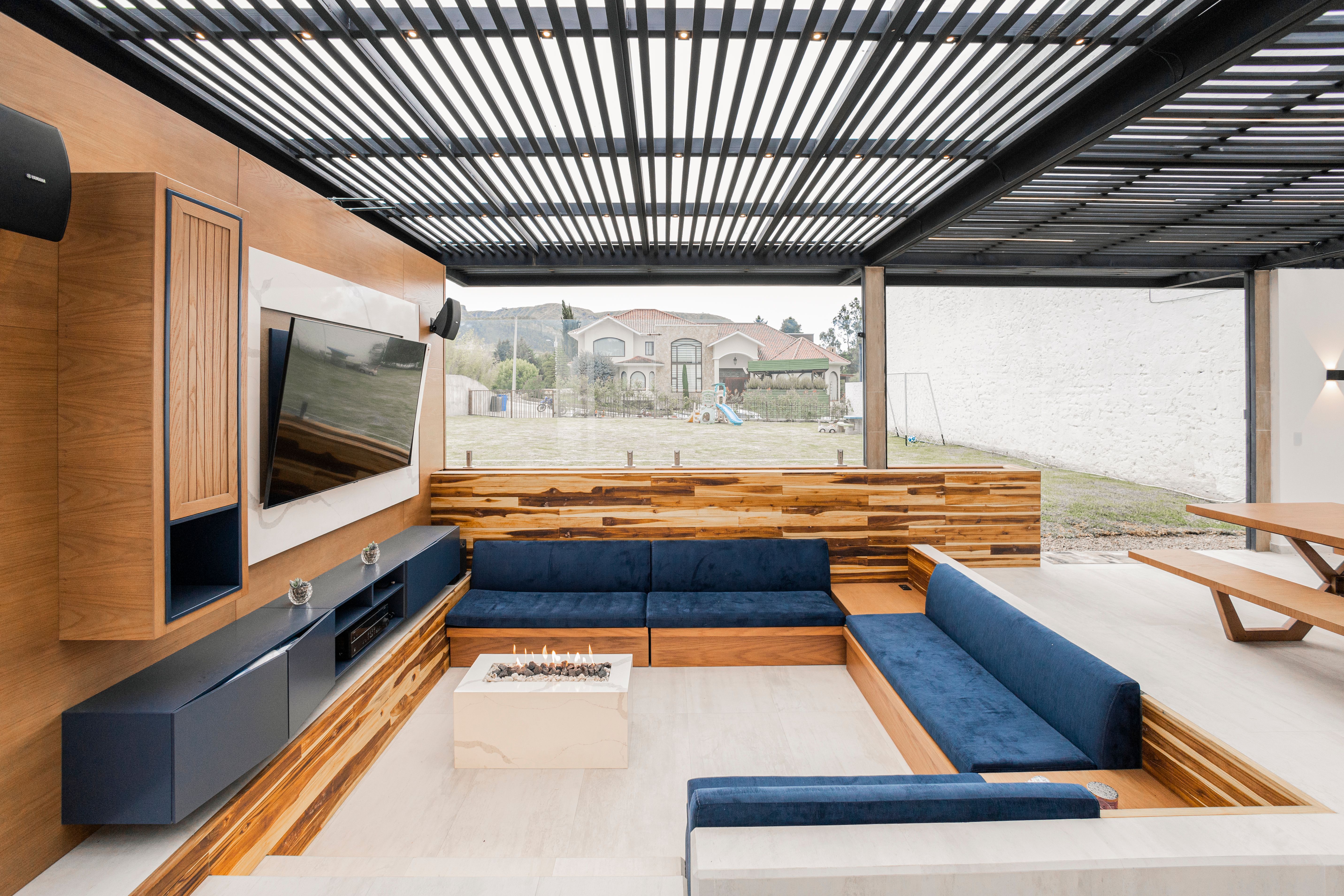 Contemporary outdoor living room with a blue sofa, warm wood details, and glass doors